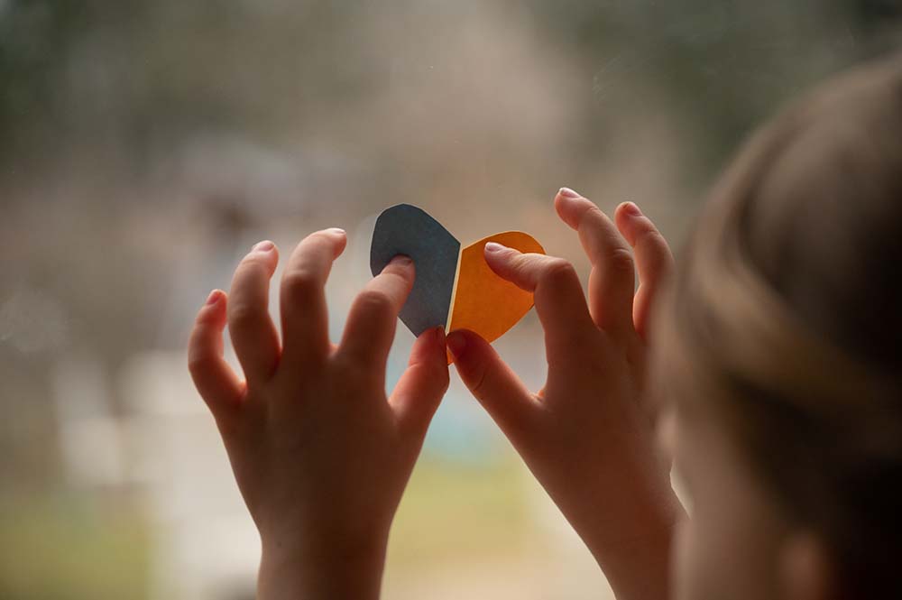 a childs hands pressing two halves of a paper heart onto a glass window